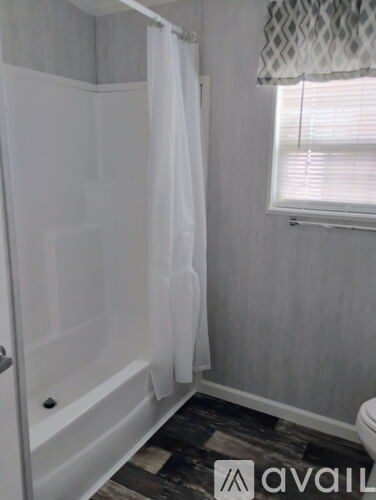 A bathroom with a white shower curtain and a window with blinds.