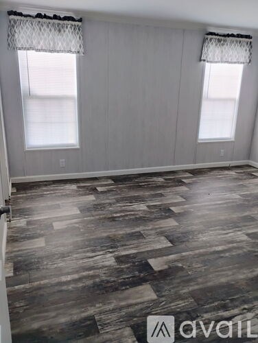 A room with wooden flooring and two windows.