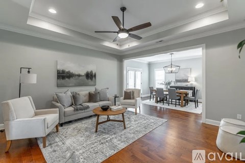 A living room with a white chair, a grey couch, a coffee table, and a dining table with chairs.