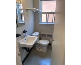 A bathroom with a toilet, sink, and window.