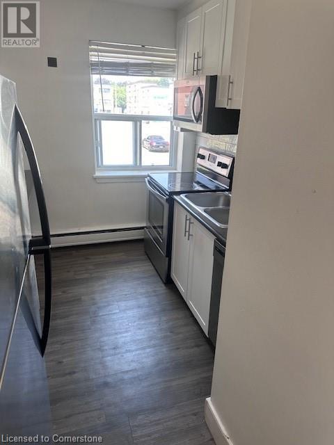 A kitchen with a fridge on the left and a window in the middle.