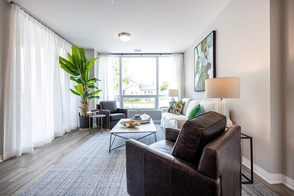 A living room with a brown leather couch and a large window with white curtains.
