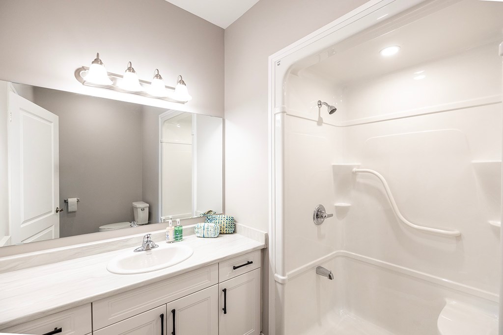 A white bathroom with a sink, mirror, and shower.