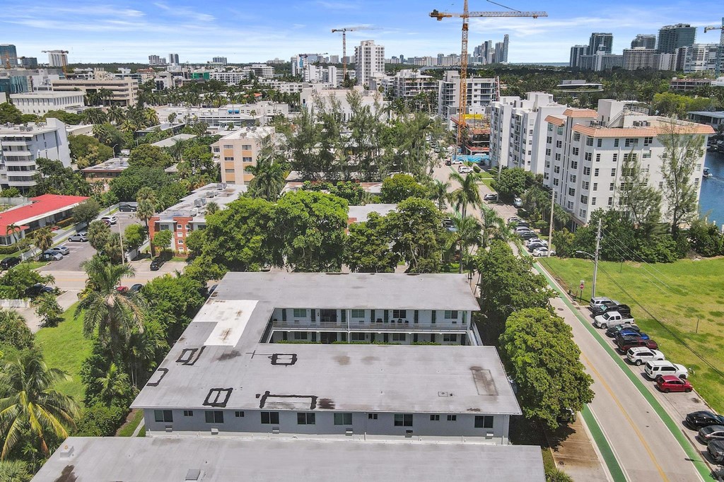 A large building with a grey roof is surrounded by trees and other buildings.