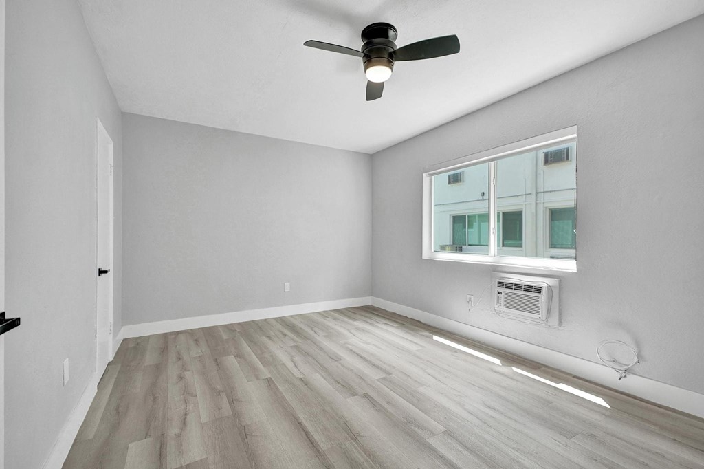 A room with a ceiling fan and a window with an air conditioner unit underneath it.