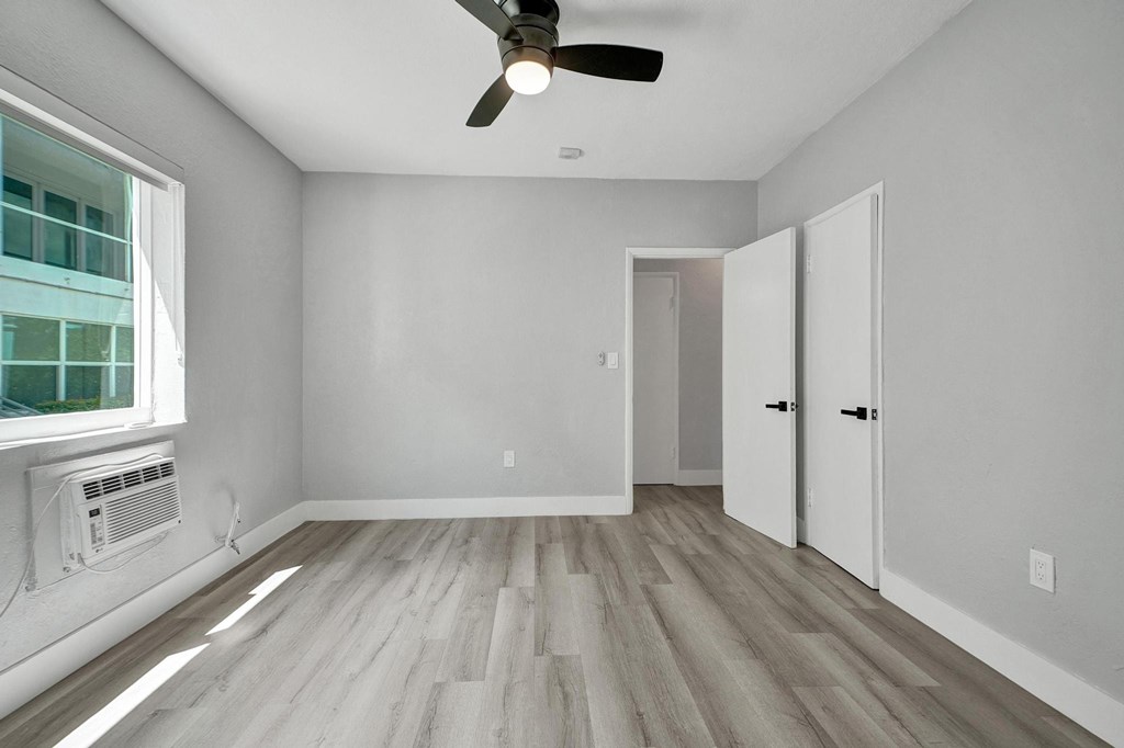 A room with a ceiling fan and a window with an air conditioner unit.