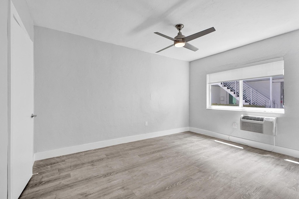 A room with a ceiling fan and a window with an air conditioner.