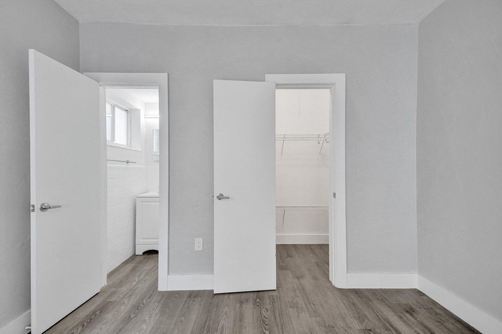Three white doors open to a hallway and a bedroom.
