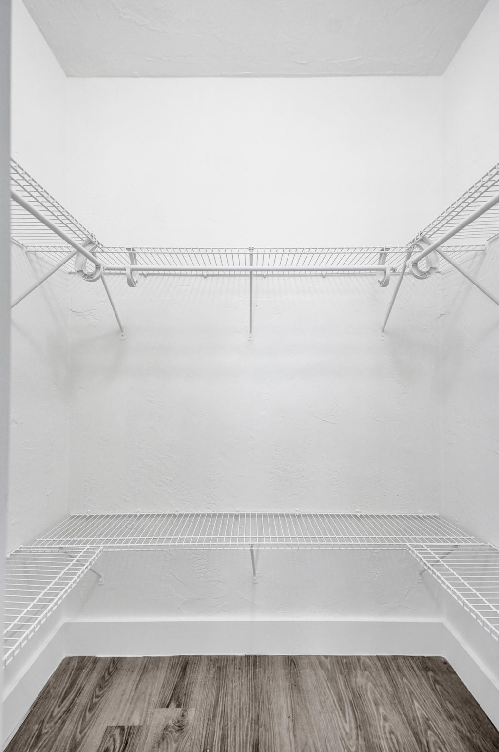 Empty walk-in closet with white walls and wooden floor.