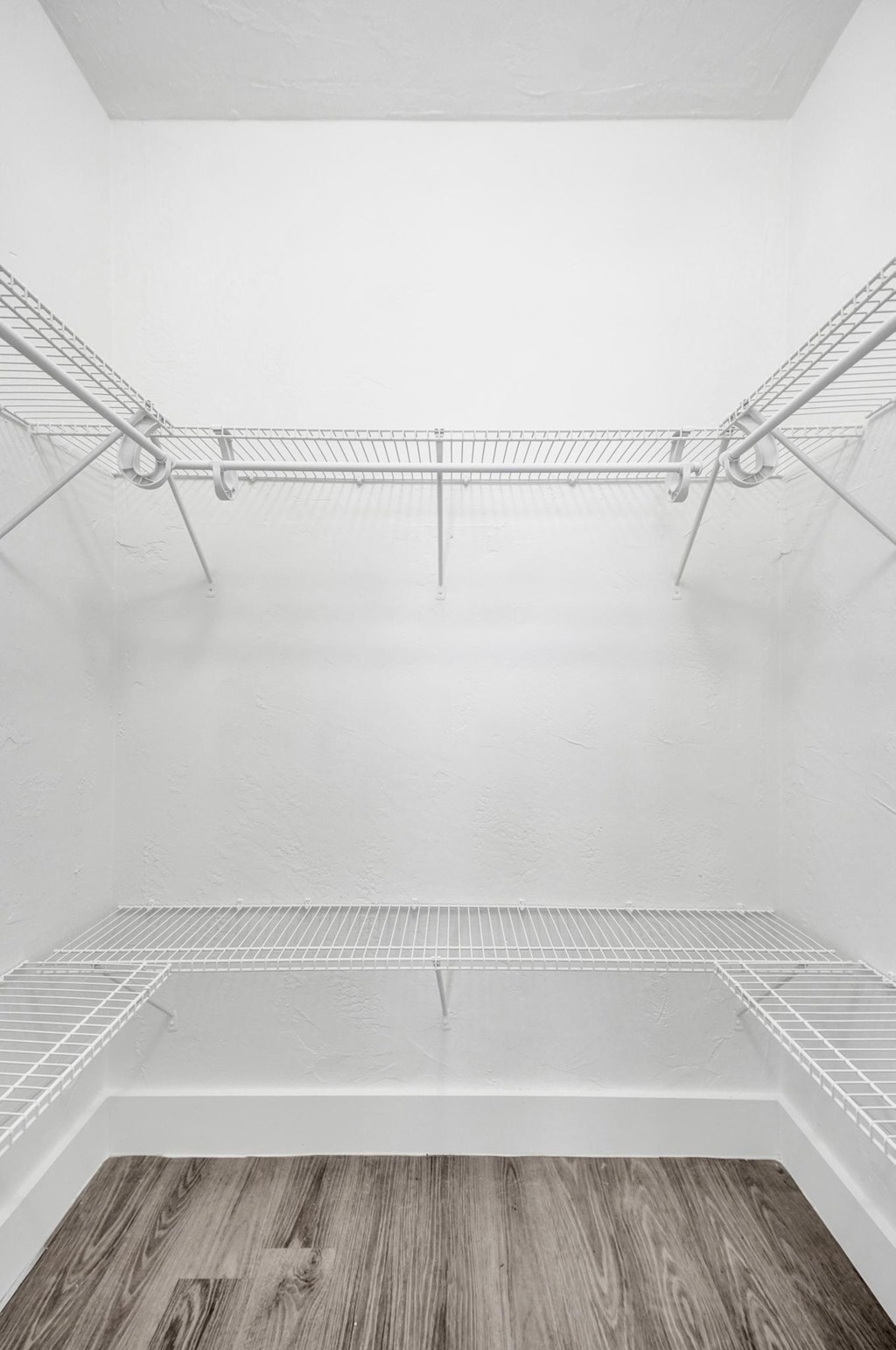 A white walk in closet with a wooden floor.