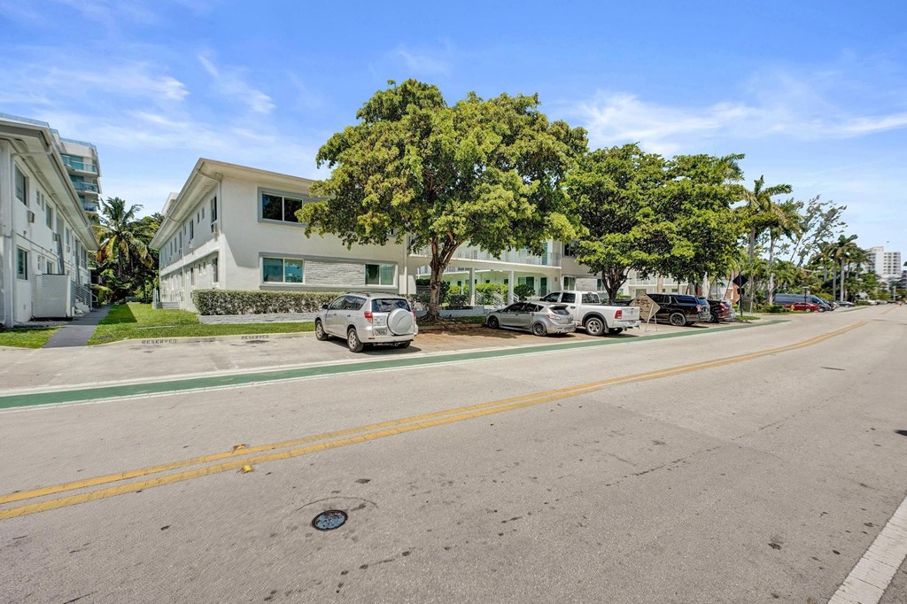 A street view with cars parked on the side and a white building in the background.