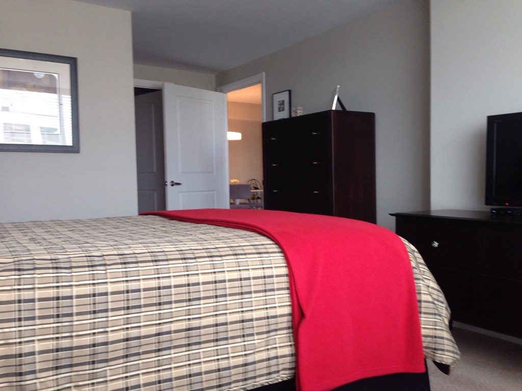 A bed with a plaid comforter and a red blanket.