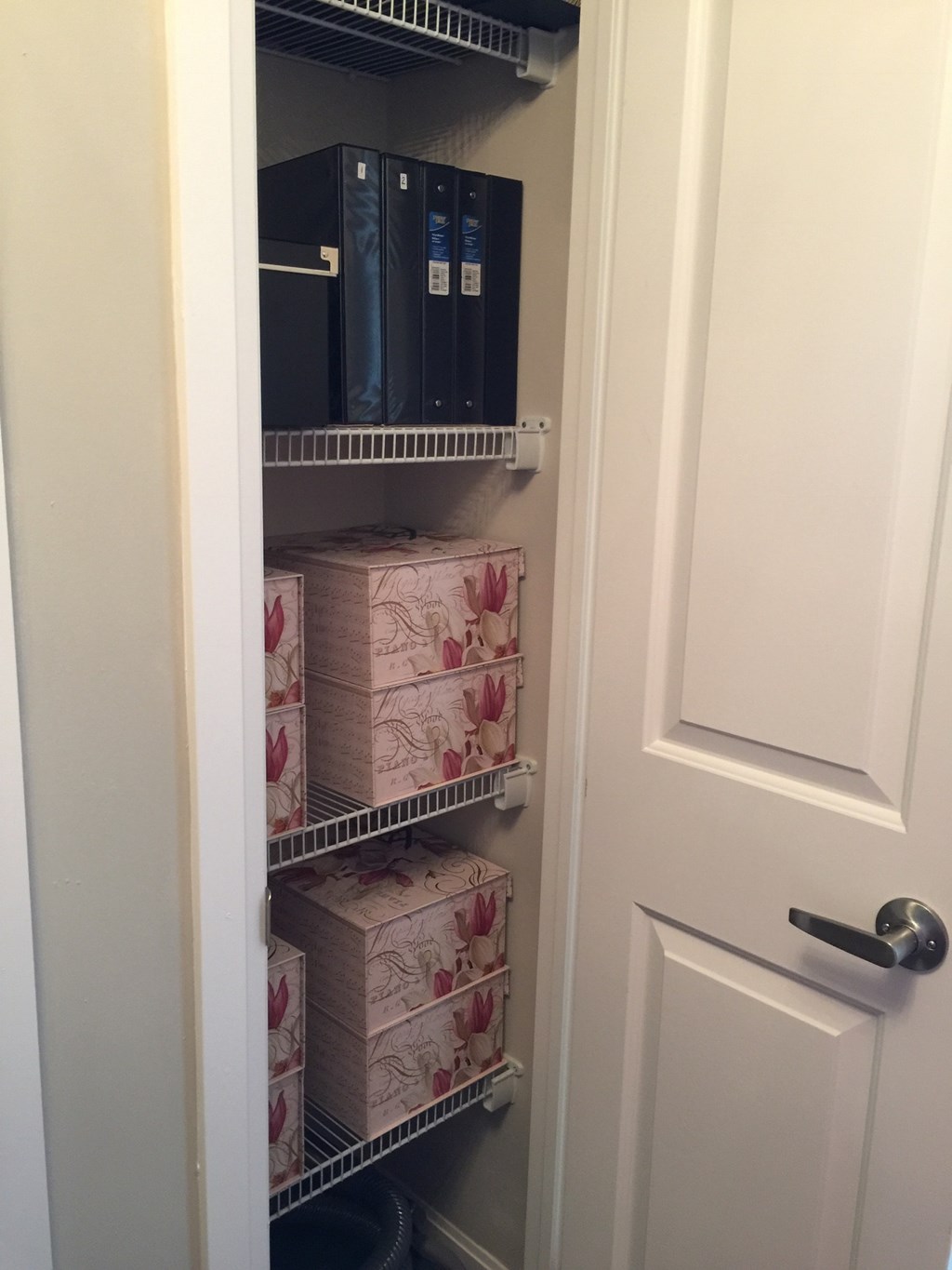 A white door is open to a pantry with a black filing cabinet and a shelf with boxes of tissues.
