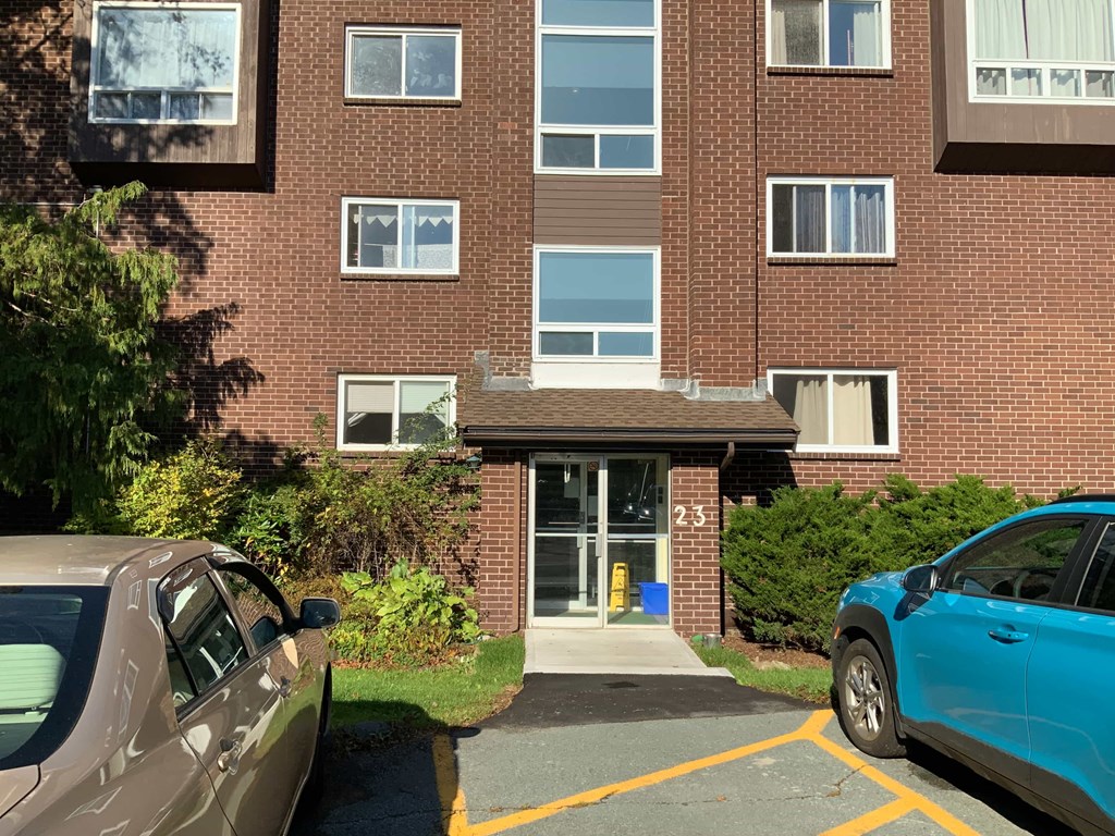 A brown car is parked in front of a brick building with the number 23 on the door.