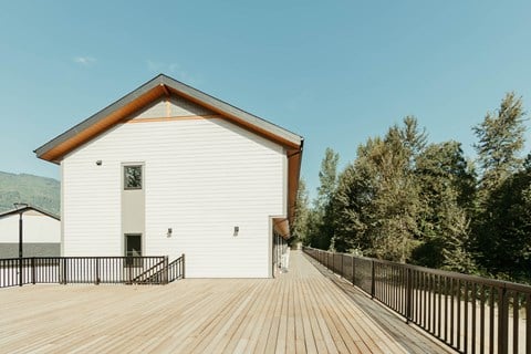 A white building with a brown roof and a wooden deck in front.