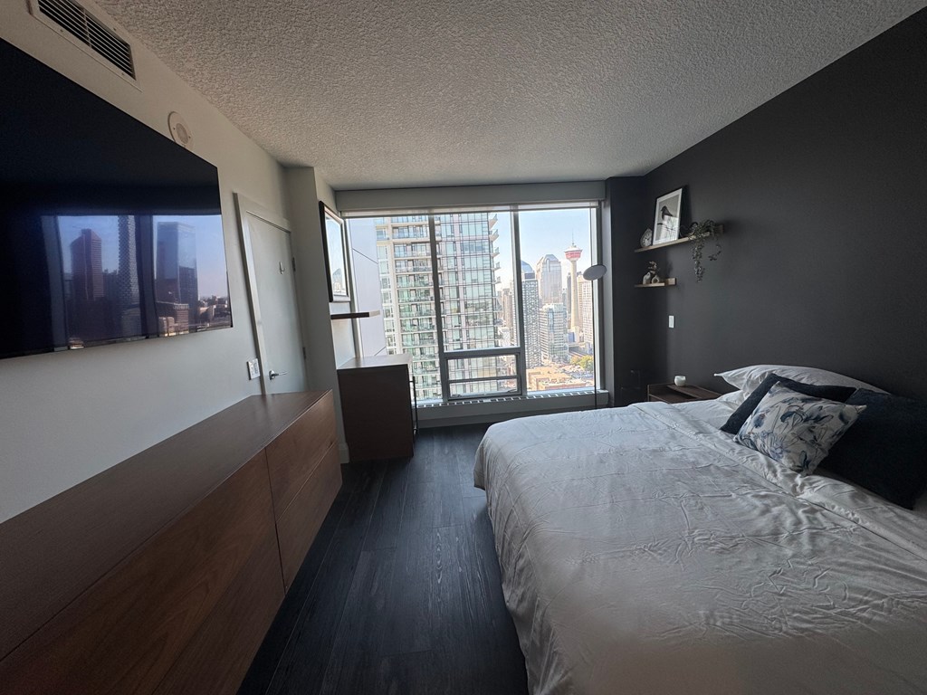 A bedroom with a large bed and a city view through the window.