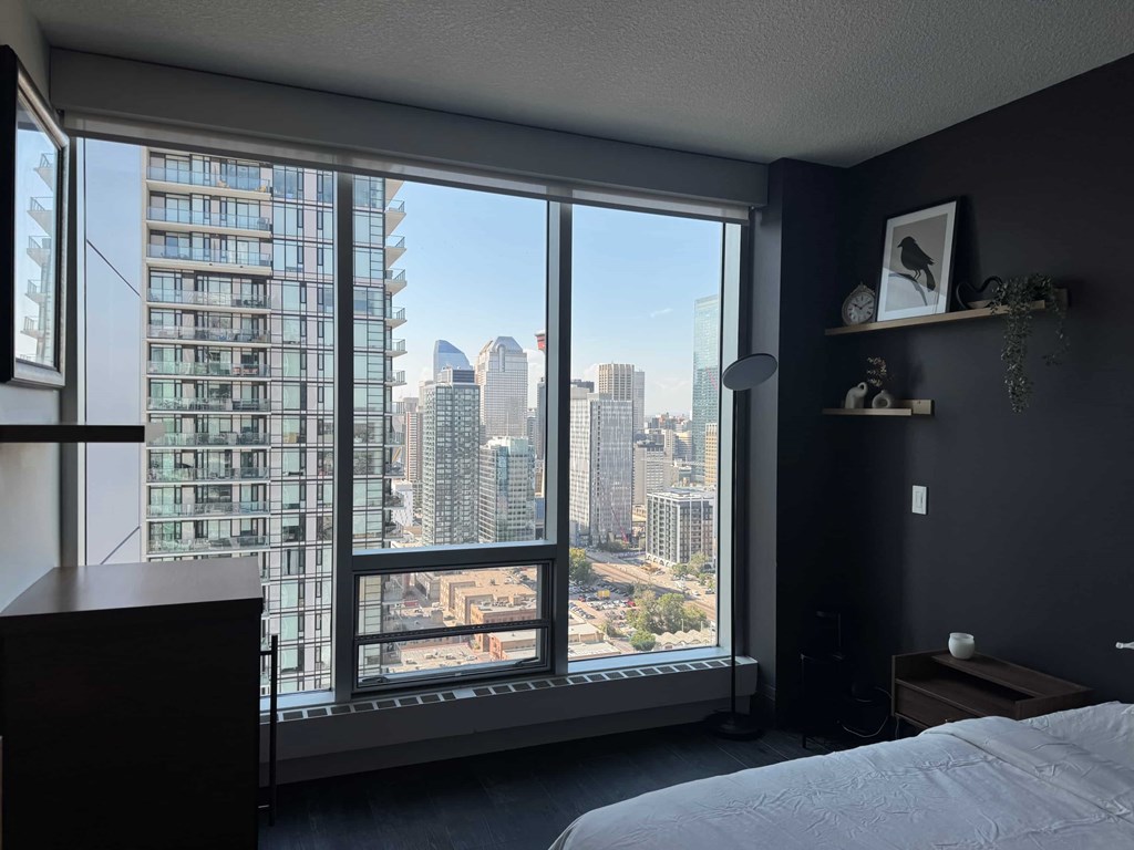 A bedroom with a large window overlooking a city skyline.