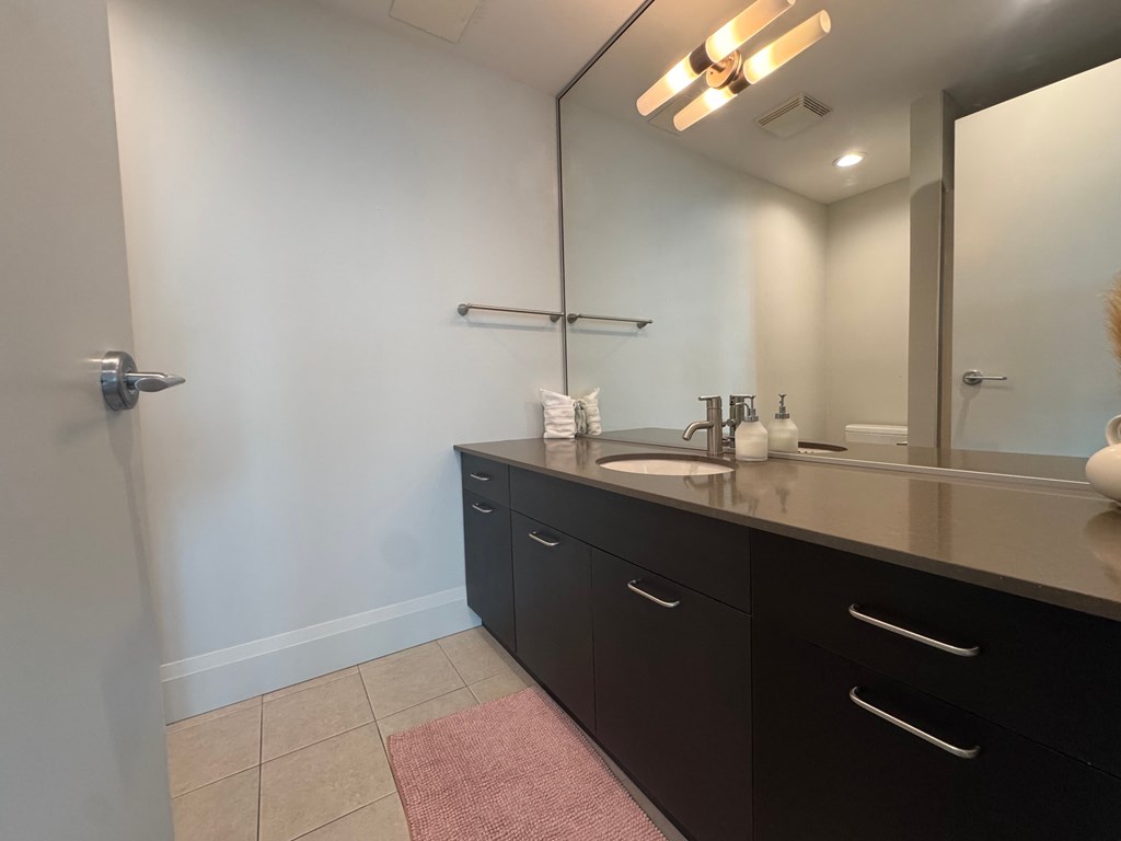 A bathroom with a sink, mirror, and a pink rug.