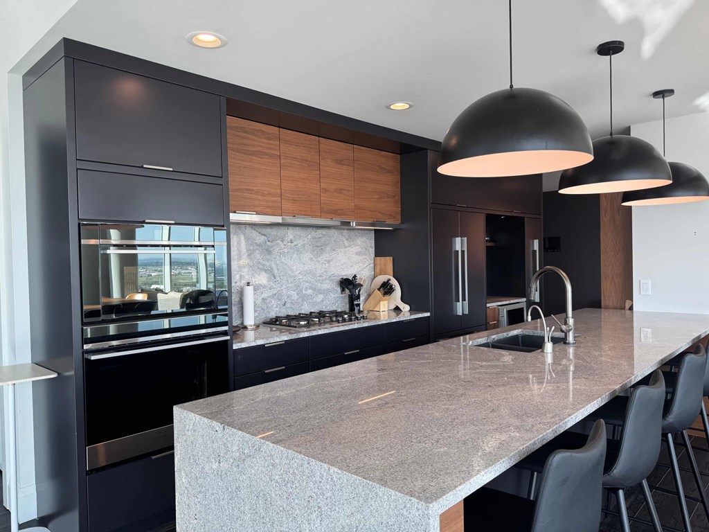 A modern kitchen with dark cabinets and a marble countertop.