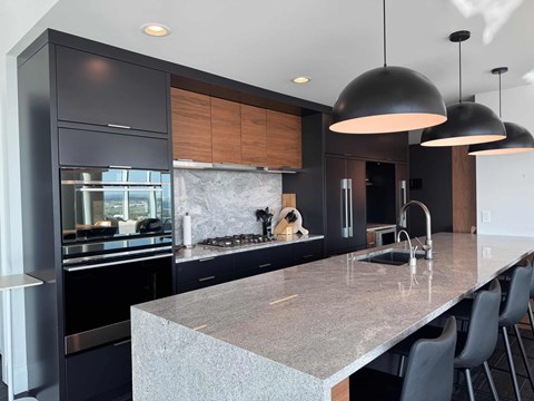 A modern kitchen with dark cabinets and a marble countertop.