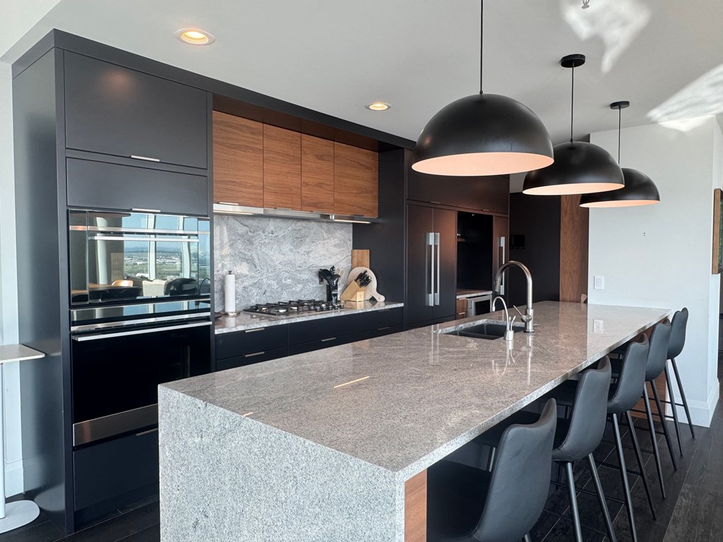 A modern kitchen with a marble countertop and black chairs.