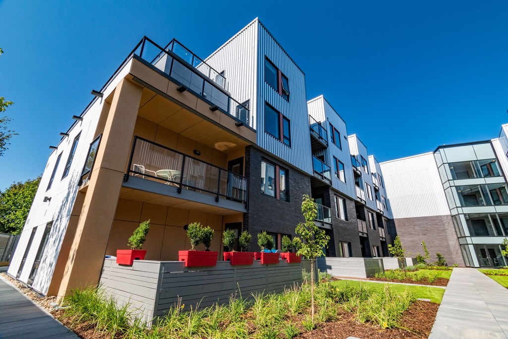 A modern building with a balcony and a small garden in front.