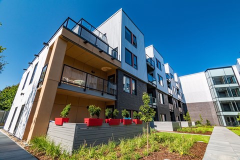 A modern building with a balcony and a small garden in front.