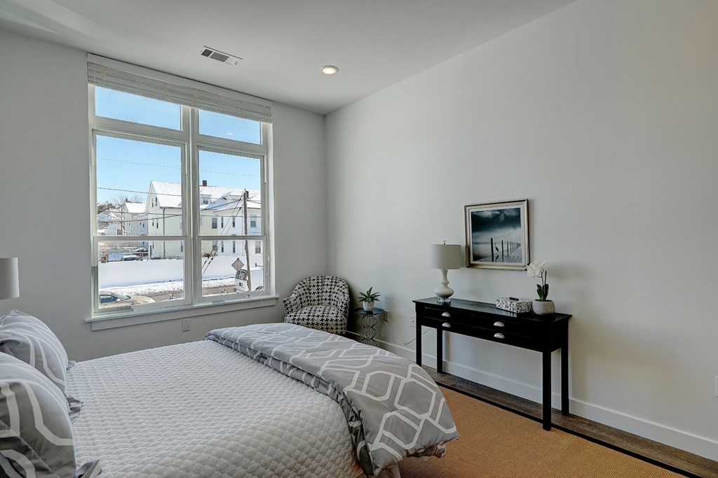A bedroom with a large bed and a table with a lamp on it.