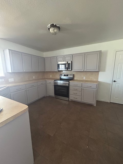 A kitchen with white cabinets and brown flooring.