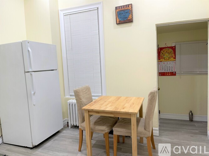 A kitchen with a white fridge, a table with chairs and a calendar on the wall.