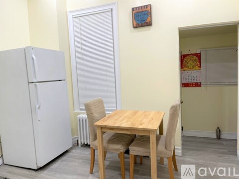 A kitchen with a white fridge, a table with chairs and a calendar on the wall.