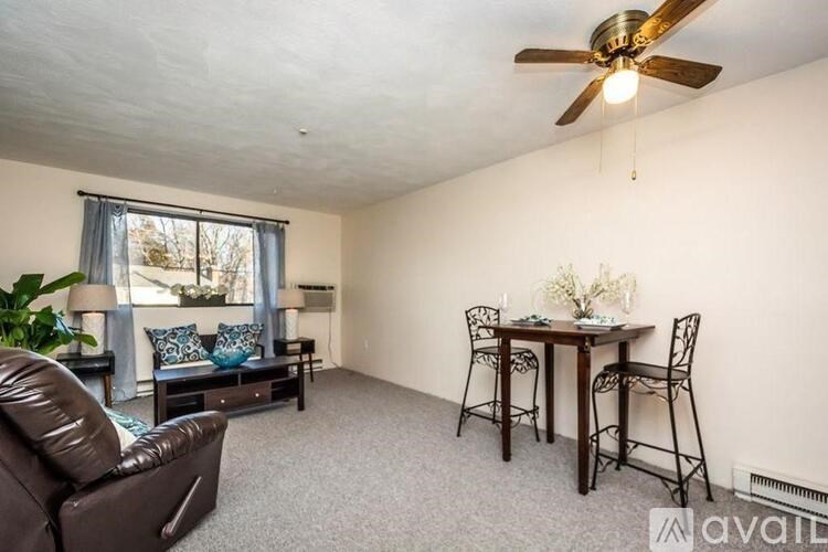 A living room with a brown leather couch, a dining table with chairs, and a ceiling fan.