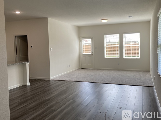 A spacious room with wooden flooring and a large window with blinds.