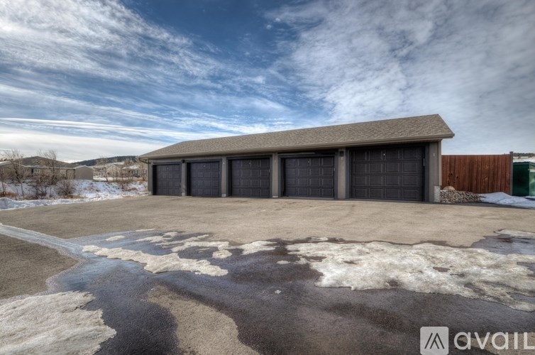 A large garage with a brown roof and four black doors is surrounded by a snowy landscape.
