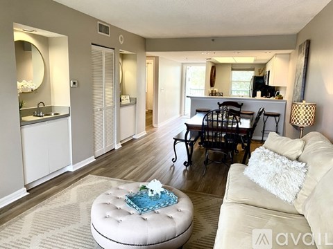 A living room with a white couch and a round ottoman with a blue cushion on it.