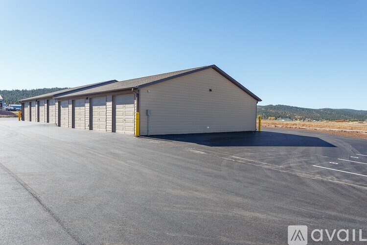 A large, grey, single-story building with a garage door is situated in a parking lot.