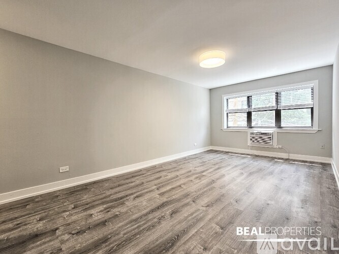 A spacious room with wooden flooring and a window with blinds.