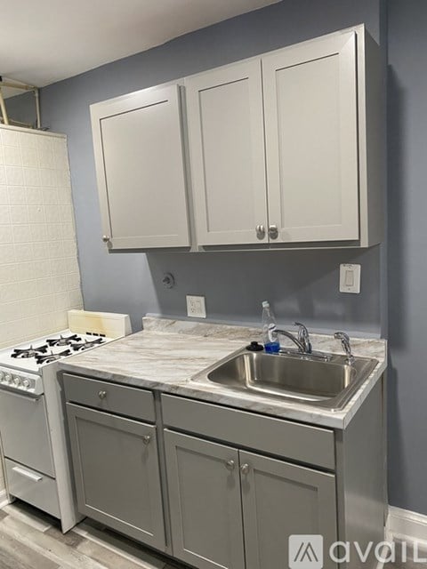 A kitchen with a white stove top oven, a white sink, and a white counter top.