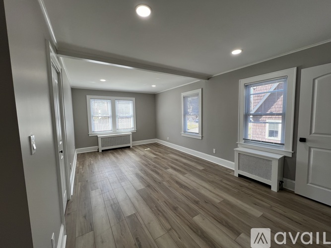 A room with wooden flooring and two windows.