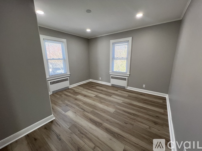 A room with wooden flooring and two windows.