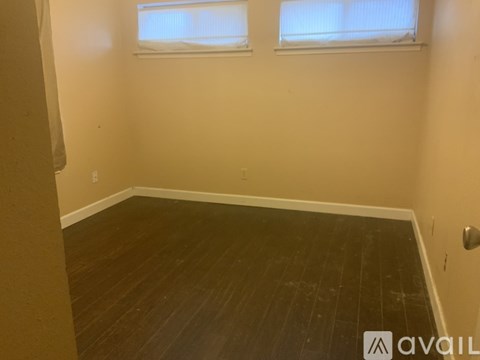 A room with wooden flooring and two windows.