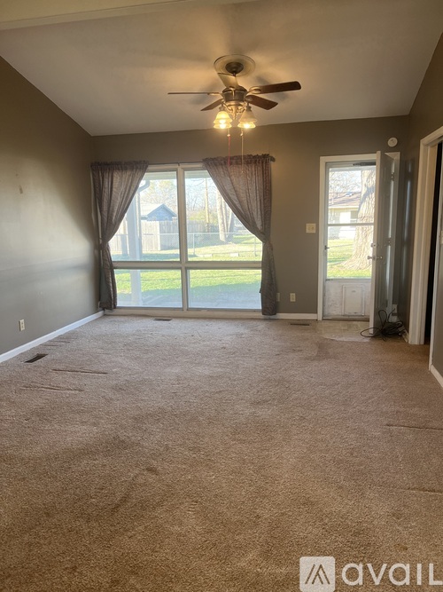 A room with a carpeted floor, a ceiling fan, and sliding glass doors leading to a backyard.