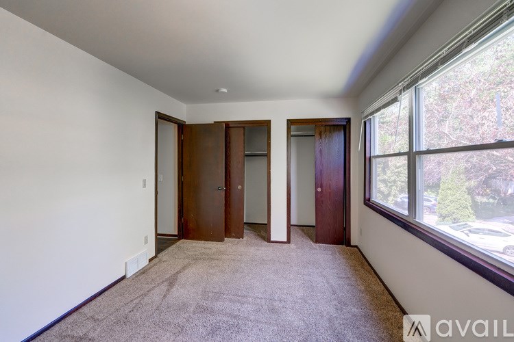 A room with a carpeted floor, two doors, and a window overlooking a parking lot.