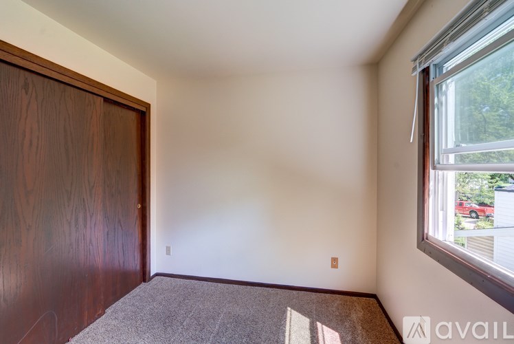 A room with a carpeted floor, a wooden door, and a window showing a red car outside.