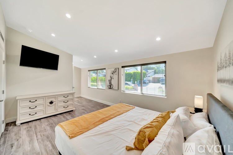 A bedroom with a large bed, a TV, and a window with blinds.