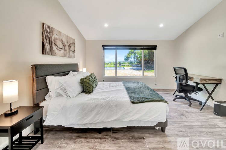 A bedroom with a large bed, a desk with a chair, and a painting on the wall.