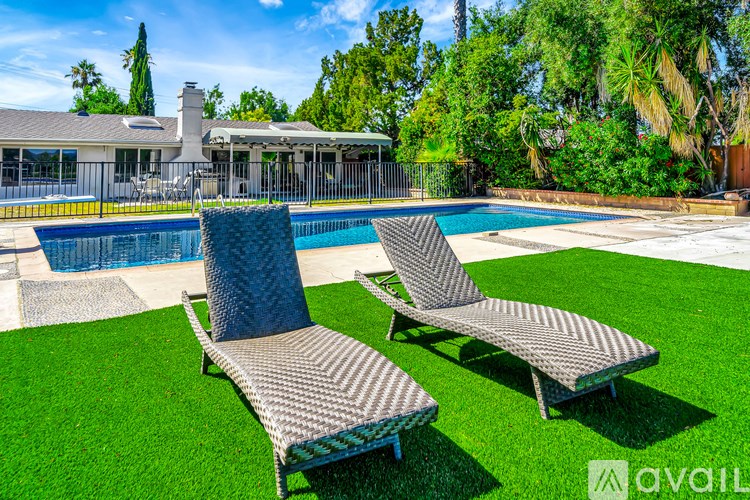 Two lounge chairs are placed on a green lawn next to a swimming pool.