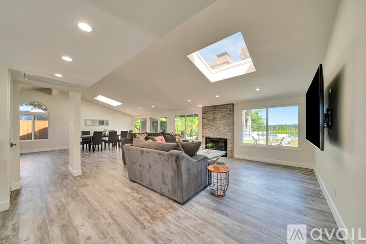 A spacious living room with a grey sofa and a flat-screen TV mounted on the wall.