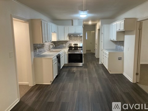 A spacious kitchen with white cabinets and a dark wood floor.