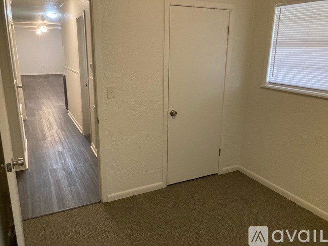 A hallway with a carpeted floor, white walls, and a closed door.
